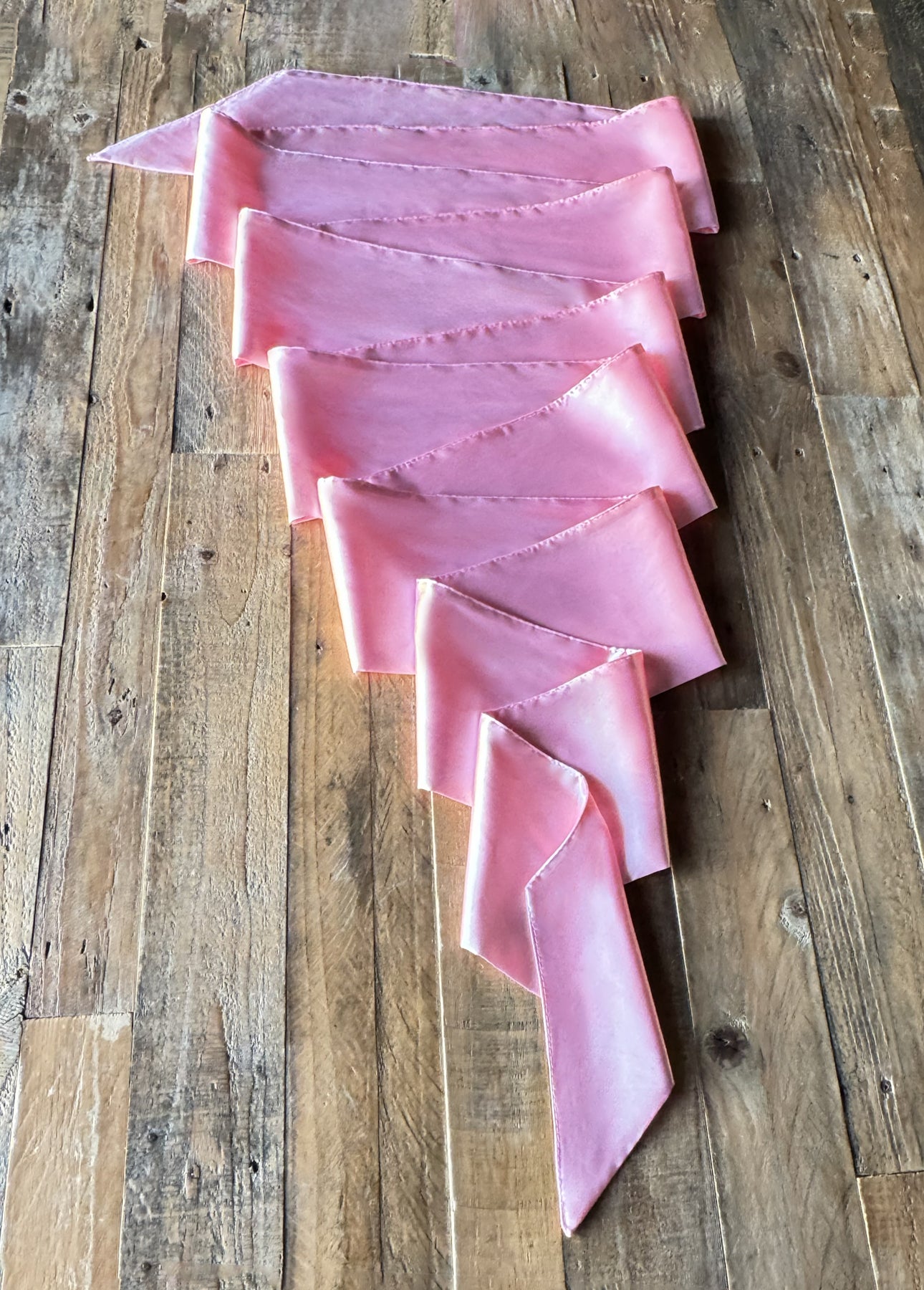 A pink satin ribbon rests elegantly on a wooden floor, ideal for enhancing sensation play experiences